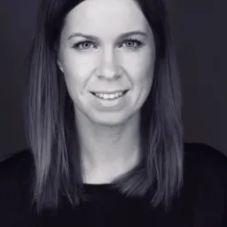 Portret uśmiechniętej kobiety z prostymi, ciemnymi włosami do ramion, na czarno-białym zdjęciu z ciemnym tłem.