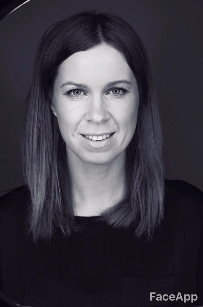 Portret uśmiechniętej kobiety z prostymi, ciemnymi włosami do ramion, na czarno-białym zdjęciu z ciemnym tłem.