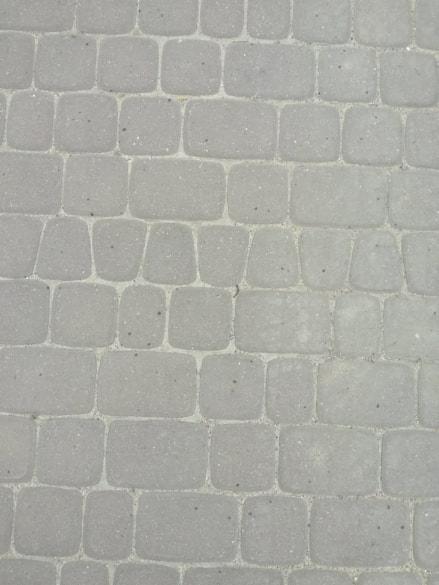 Szara, ułożona kostka brukowa w regularnym wzorze, widok z góry.
