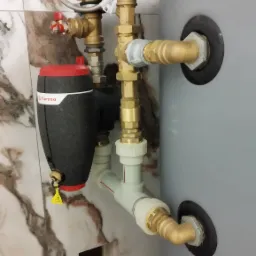 Szary zbiornik z podłączeniami hydraulicznymi z zaworami i filtrem Flamco na tle marmurowej ściany.