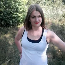 Kobieta z czerwonymi ustami w białym podkoszulku, pozująca na tle zarośli w słoneczny dzień, z widocznym logo Camera360 w rogu.