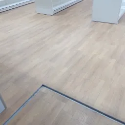 Nowa, pusta przestrzeń biurowa z drewnopodobną podłogą i białymi regałami sklepowymi, widoczny fragment metalowej ramy w podłodze z napisem 'ULTIMUS (A95 x 80)'.