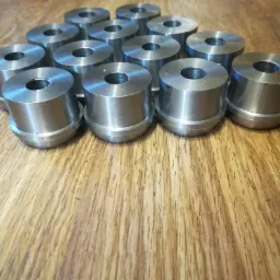 Szereg metalowych tulejek z centralnym otworem, ułożonych na drewnianej powierzchni, widoczne ślady obróbki skrawaniem wewnątrz otworu.