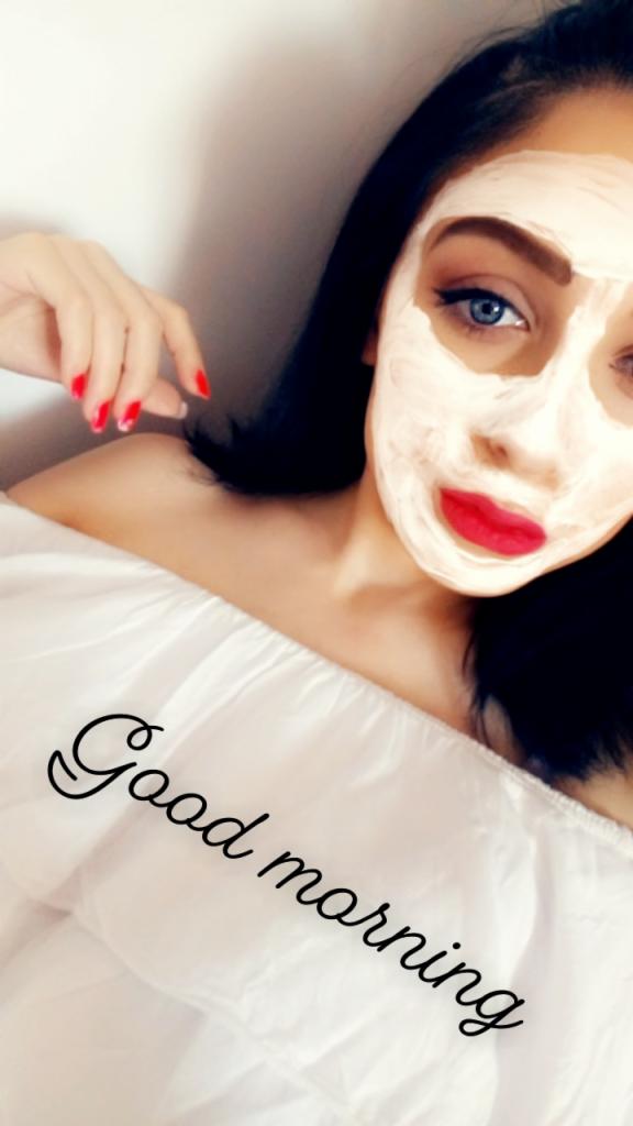 Portret kobiety z maseczką na twarzy, czerwone usta i pomalowane paznokcie. Widoczny napis 'Good morning' na białej bluzce.