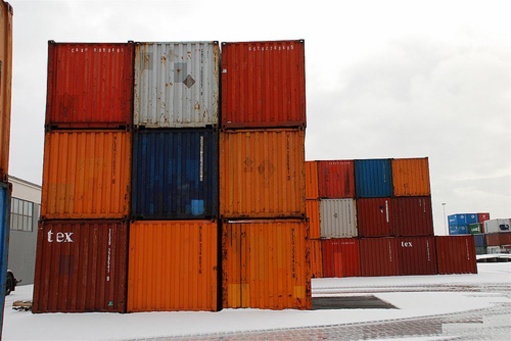 Ułożone w stosy, kolorowe kontenery transportowe na ośnieżonym placu składowym pod pochmurnym niebem.