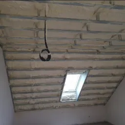Poddasze ocieplone pianką PUR z widoczną konstrukcją metalową, okno dachowe i zwisający kabel.