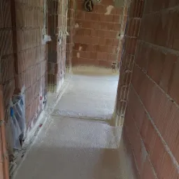 Poddasze w trakcie ocieplania pianką PUR, widoczne ceglane ściany i świeżo nałożona warstwa izolacji, z widocznymi instalacjami elektrycznymi.