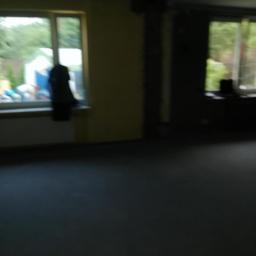 Imbud - Wnętrze w trakcie prac remontowych: surowe ściany, okna z widokiem na zieleń, ciemna podłoga i widoczne elementy konstrukcyjne stropu.