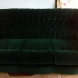 Zielona, aksamitna sofa z drewnianymi zdobieniami na bokach i pikowanym oparciem w romby.