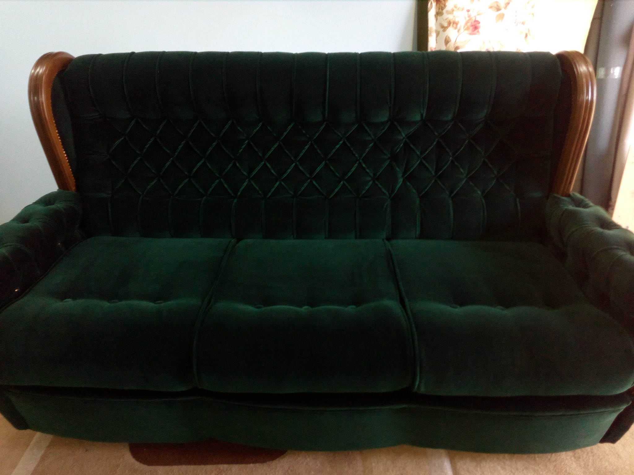 Zielona, aksamitna sofa z drewnianymi zdobieniami na bokach i pikowanym oparciem w romby.