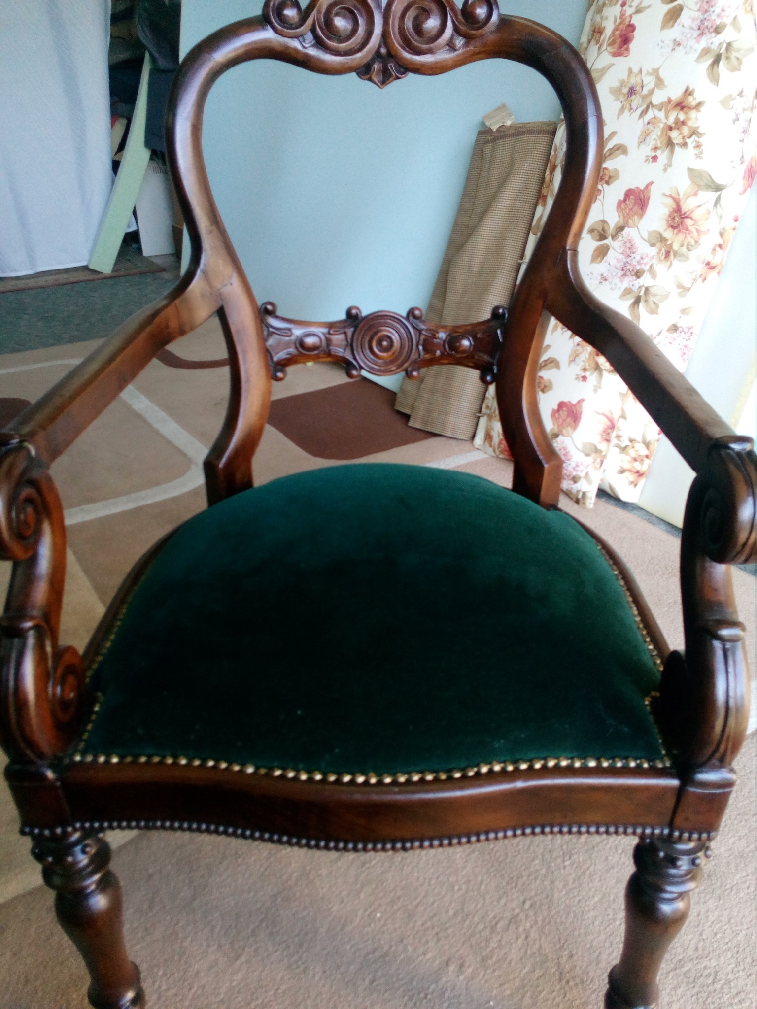 Odrestaurowany fotel z ciemnozielonym, aksamitnym siedziskiem, drewnianą ramą z dekoracyjnymi rzeźbieniami i ozdobnymi gwoździami tapicerskimi wzdłuż krawędzi.