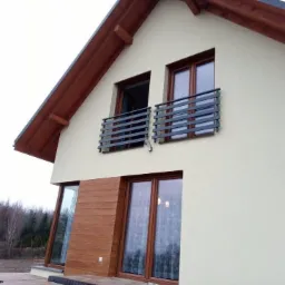 Elewacja domu jednorodzinnego z dwoma balkonami zabezpieczonymi nowoczesnymi, poziomymi balustradami ze stali nierdzewnej w kolorze grafitowym, z widocznymi mocowaniami.