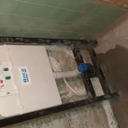 Stelaż podtynkowy WC marki Roca zamontowany w surowej łazience, widoczne instalacje hydrauliczne i fragment starej glazury.