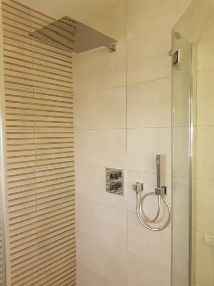 Nowoczesna kabina prysznicowa z deszczownicą i panelem sterowania, wykończona beżowymi płytkami z dekoracyjnym wzorem.