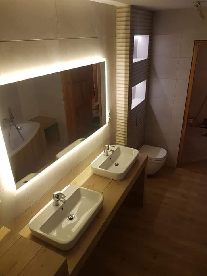 Nowoczesna łazienka z dwoma umywalkami nablatowymi na drewnianym blacie, podświetlane lustro LED, płytki ceramiczne na ścianach i drewniana podłoga.