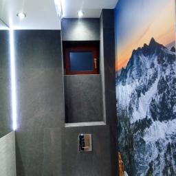 ANMIL-FLIZ - Nowoczesna łazienka z szarą, matową okładziną ścienną, podświetleniem LED i małym oknem, uzupełniona fototapetą z motywem górskim.