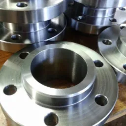 Stalowe kołnierze z otworami na śruby, ułożone na drewnianym blacie, widoczne ślady obróbki.