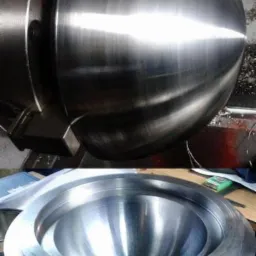 Dwie metalowe półkule, jedna obrabiana w uchwycie tokarskim, druga gotowa, z widocznymi śladami obróbki i odbiciami światła.