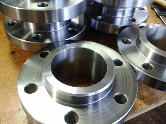 Stalowe kołnierze z otworami na śruby, ułożone na drewnianym blacie, widoczne ślady obróbki.