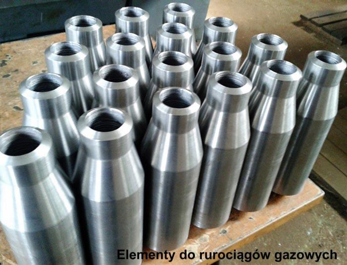 Partia metalowych elementów rurowych z gwintem wewnętrznym, ułożonych na drewnianej powierzchni, widoczne ślady obróbki.