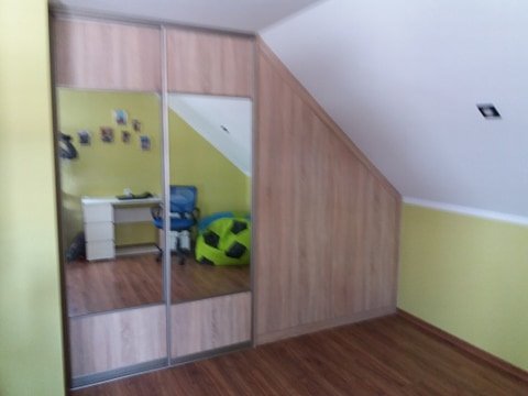 Szafa wnękowa z przesuwnymi, lustrzanymi drzwiami w pokoju na poddaszu, widoczne odbicie biurka i krzesła.