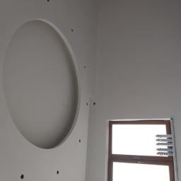 Firma Remontowo Budowlana Tomasz Piechota - Ściana w Tuszowie Narodowym z otworem w kształcie okręgu i małymi otworami na oświetlenie, okno zabezpieczone pianką montażową.