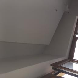 Firma Remontowo Budowlana Tomasz Piechota - Poddasze po malowaniu na biało, widoczne okno dachowe z drewnianą ramą i fragment skośnego sufitu z widocznymi punktami świetlnymi.