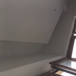 Poddasze po malowaniu na biało, widoczne okno dachowe z drewnianą ramą i fragment skośnego sufitu z widocznymi punktami świetlnymi.