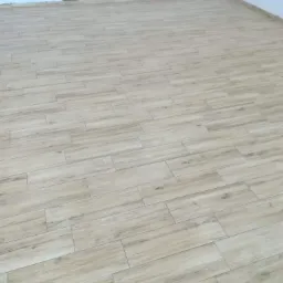 Jasne, drewnopodobne płytki gresowe ułożone na podłodze w nowym pomieszczeniu, widoczne fugi i listwy przypodłogowe w kolorze białym.