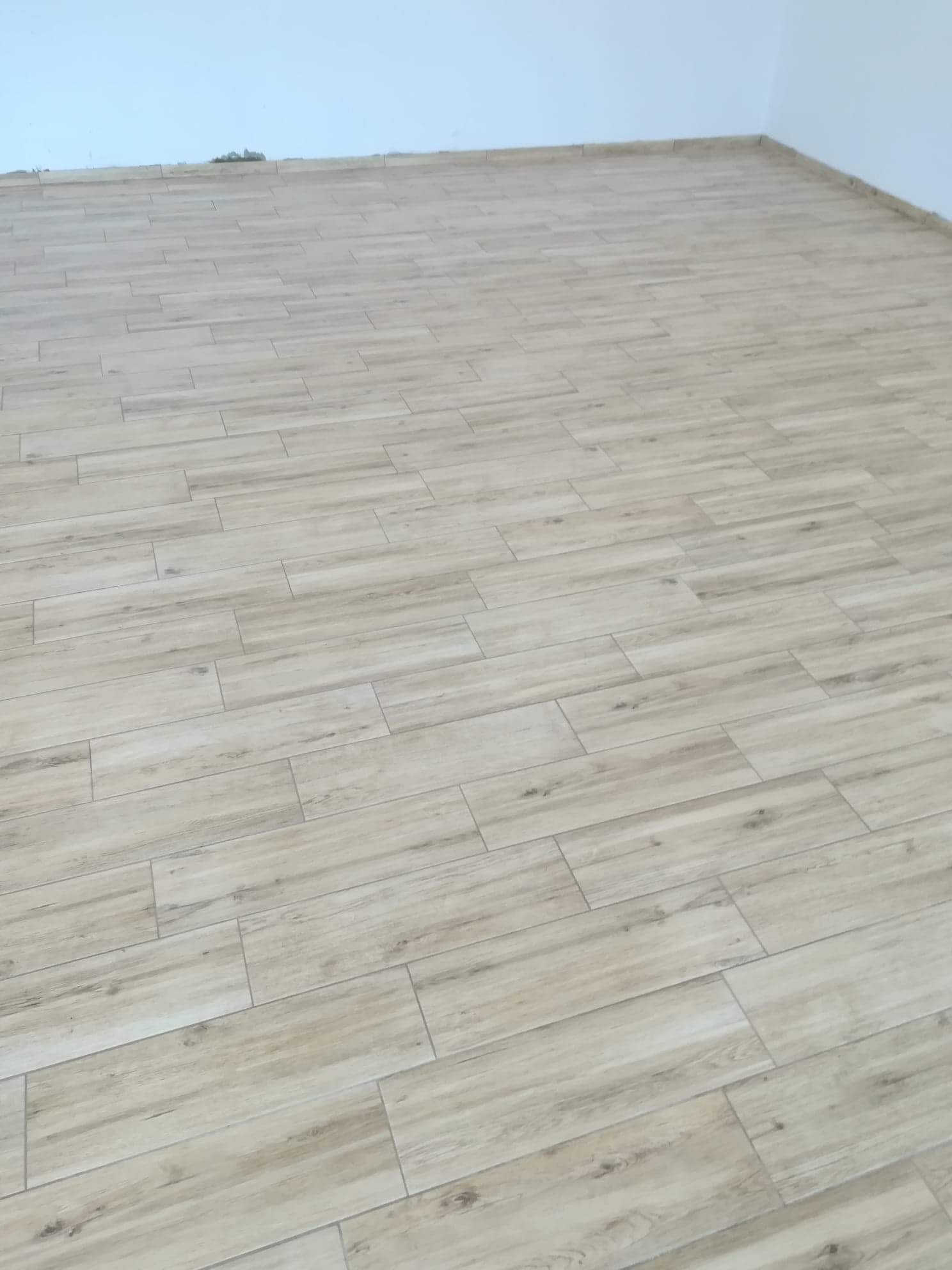 Jasne, drewnopodobne płytki gresowe ułożone na podłodze w nowym pomieszczeniu, widoczne fugi i listwy przypodłogowe w kolorze białym.