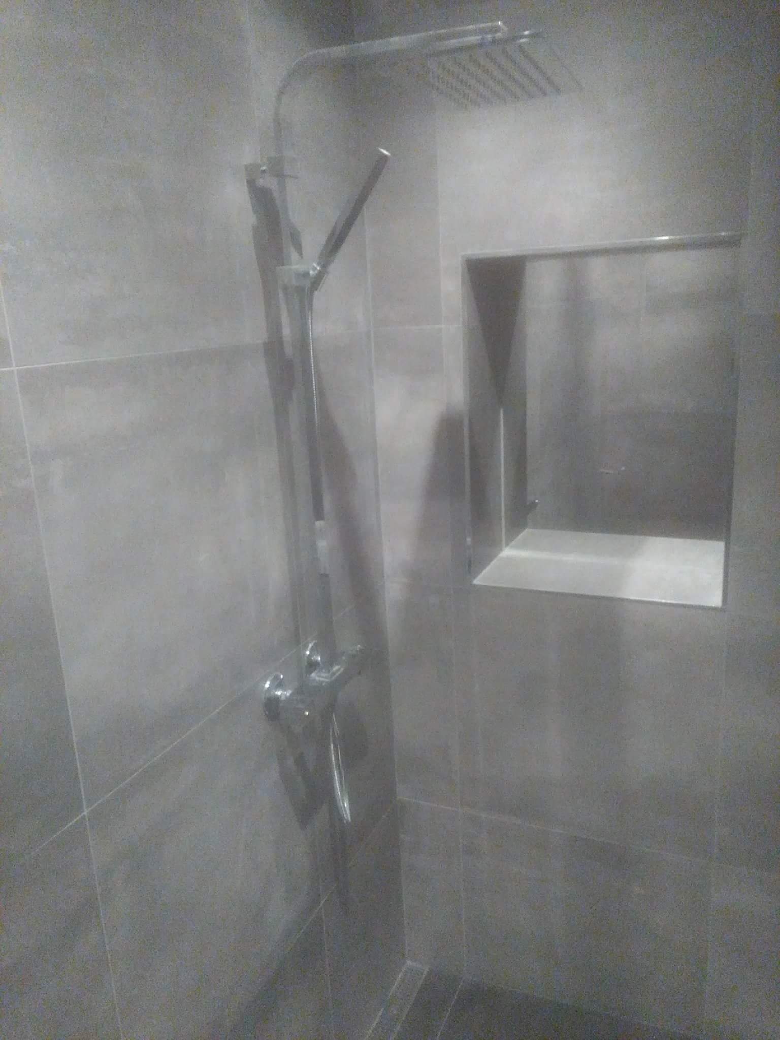 Wykończona łazienka z szarymi, wielkoformatowymi płytkami, wnęką w ścianie i chromowaną baterią prysznicową z deszczownicą.