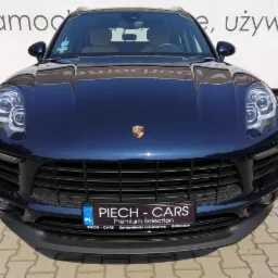 Granatowy samochód marki Porsche Macan, widok z przodu, z widocznym logo firmy Piech-Cars na tablicy rejestracyjnej i w tle napis 'Samochody używane'.
