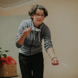 Kobieta w okularach w Żaganiu, w swetrze, prezentuje materiały edukacyjne, prawdopodobnie podczas przygotowania do lekcji.