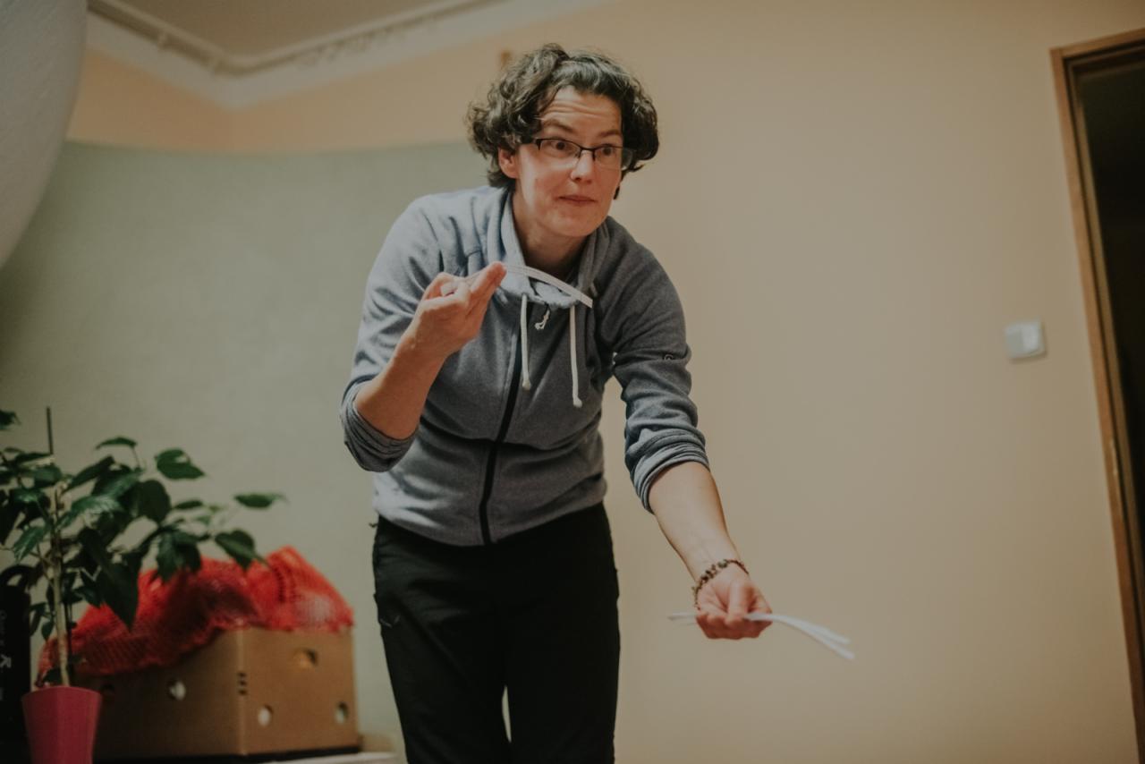 Kobieta w okularach w Żaganiu, w swetrze, prezentuje materiały edukacyjne, prawdopodobnie podczas przygotowania do lekcji.