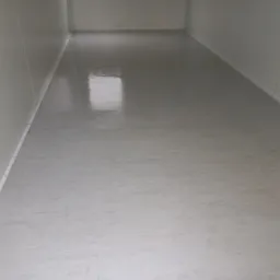 Białe, puste pomieszczenie z błyszczącą podłogą i panelowymi ścianami, widoczne łączenia paneli.