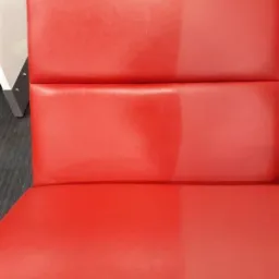 Czerwone obicie krzesła częściowo wyczyszczone, ukazujące różnicę w kolorze i fakturze przed i po czyszczeniu.