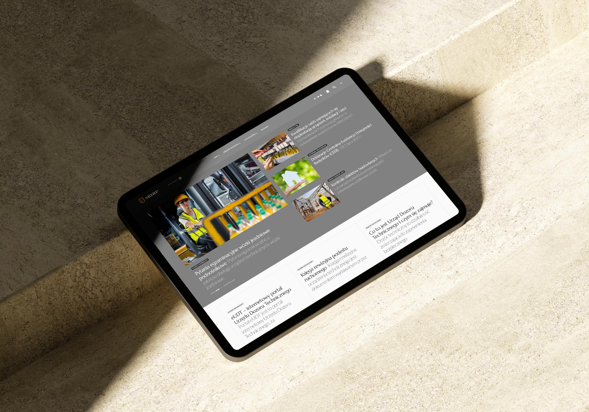 Tablet wyświetla stronę internetową sbihp.pl z artykułami dotyczącymi Urzędu Dozoru Technicznego, w tym pytania egzaminacyjne na wózki jezdniowe i informacje o eUDT.