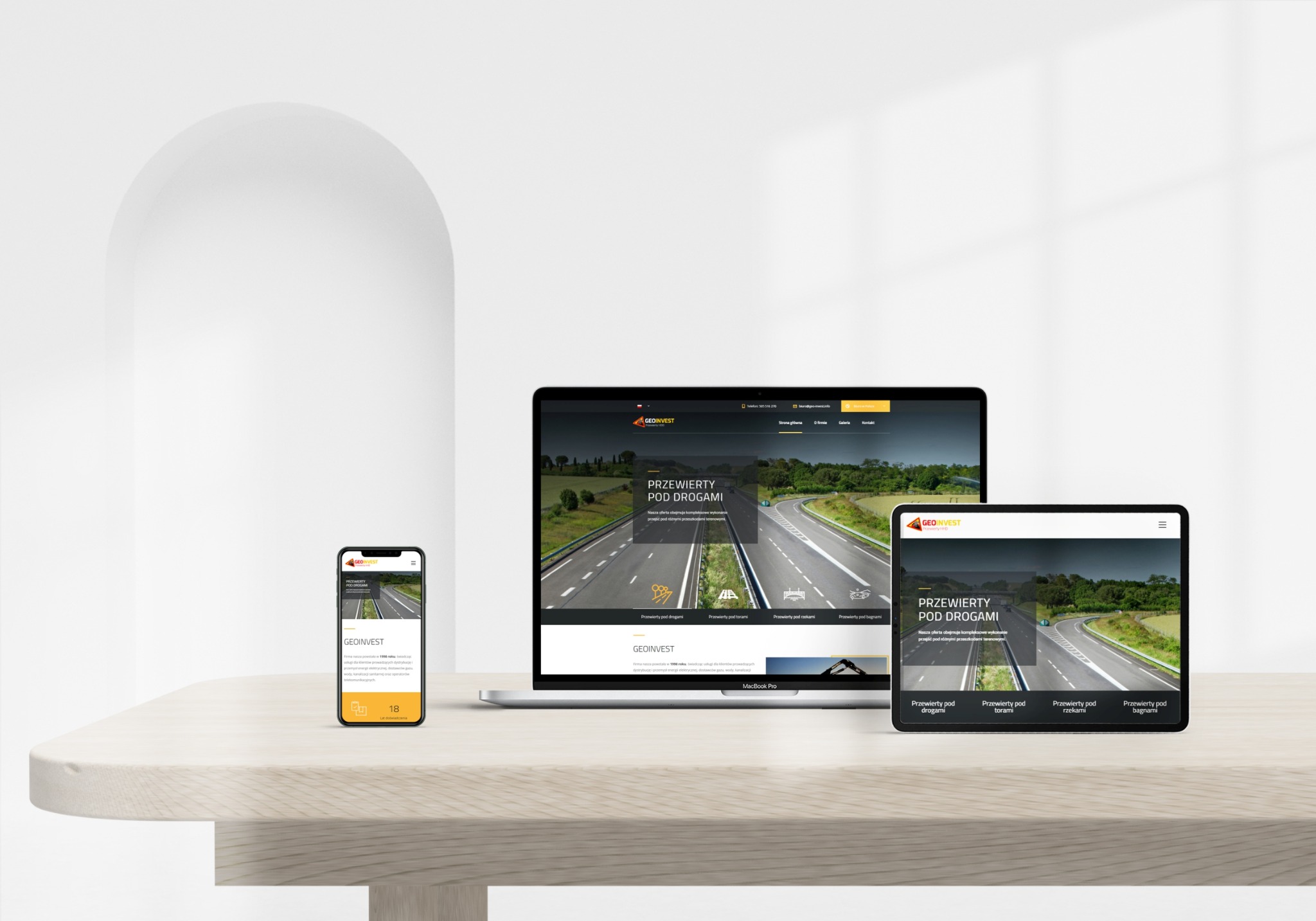Responsywna strona internetowa firmy GeoInvest wyświetlana na laptopie, tablecie i smartfonie na jasnym drewnianym stole, prezentująca ofertę przewiertów pod drogami.