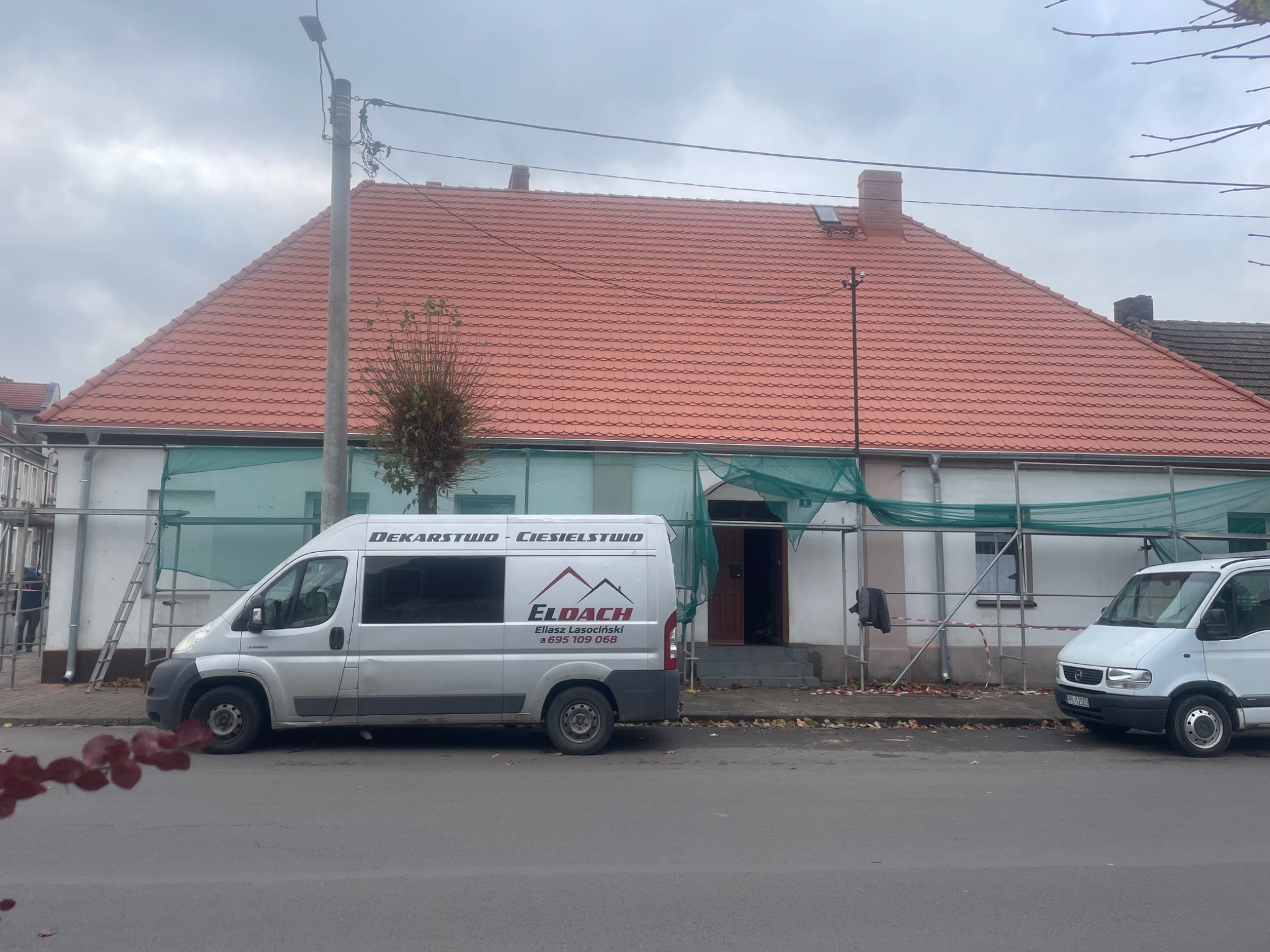 Dom z nowym, czerwonym dachem, częściowo osłonięty siatką ochronną. Na pierwszym planie samochód dostawczy z logo firmy dekarskiej Eldach.