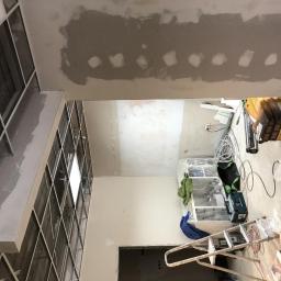 Usługi Budowlane Dariusz Lewandowski - Wnętrze w trakcie remontu: widok na sufit z metalową konstrukcją podwieszaną, częściowo pokryty płytami gipsowymi, ściany w trakcie szpachlowania, widoczne narzędzia i materiały budowlane.