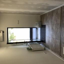 Usługi Budowlane Dariusz Lewandowski - Pokój w trakcie remontu: ściany przygotowane pod malowanie, widoczny grzejnik, okno, oraz fragment ściany wyłożonej płytkami imitującymi drewno.