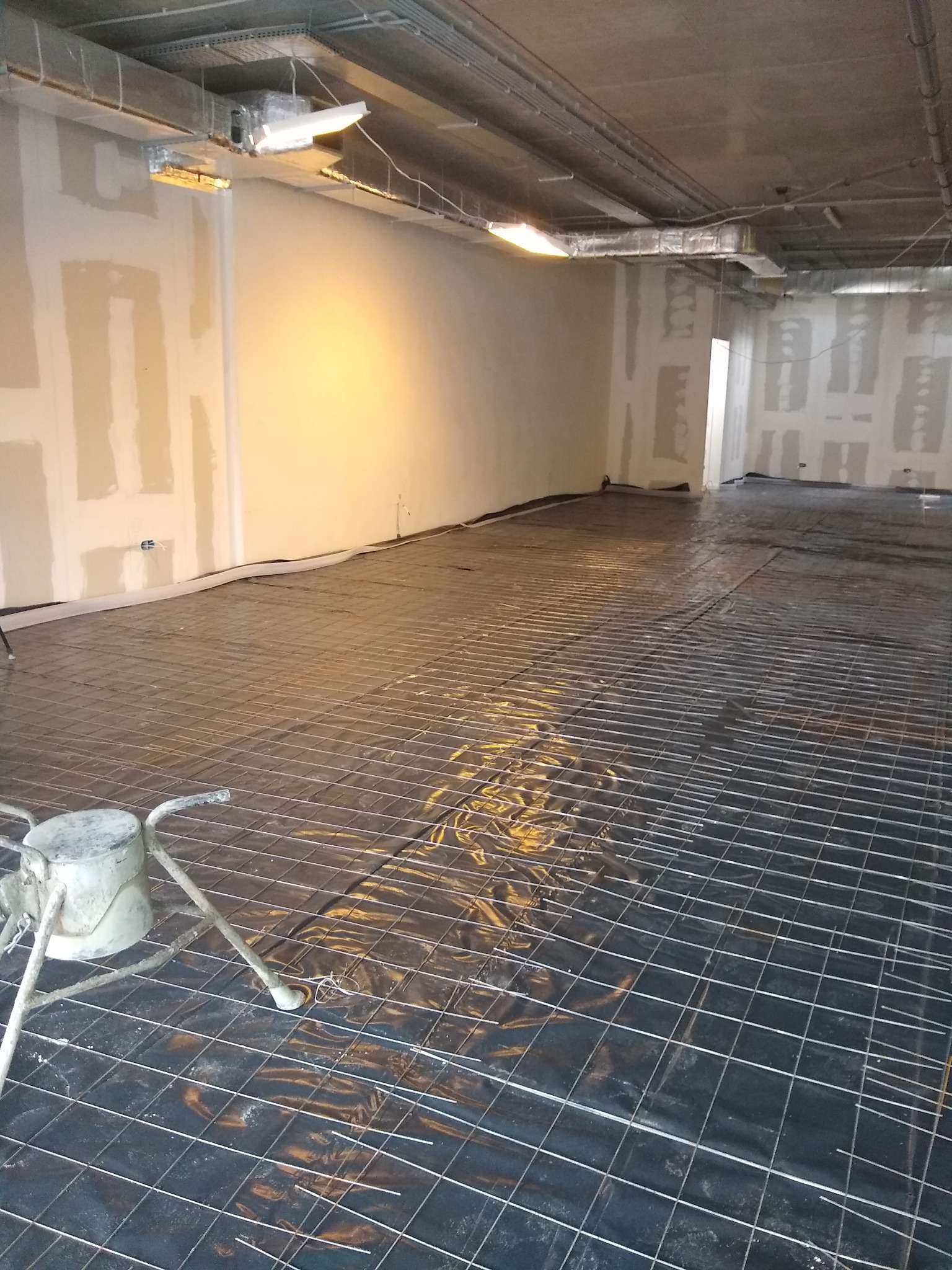 Przygotowanie podłoża pod wylewkę: rozłożona siatka zbrojeniowa na folii, widoczny stojak z pojemnikiem na zaprawę, surowe ściany w tle.