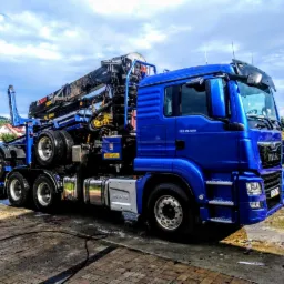 Niebieska ciężarówka MAN z żurawiem hydraulicznym, model TGS 26.500, na placu budowy. Widoczny fragment budynku w tle. Żuraw marki GLANGLIFT 2515.