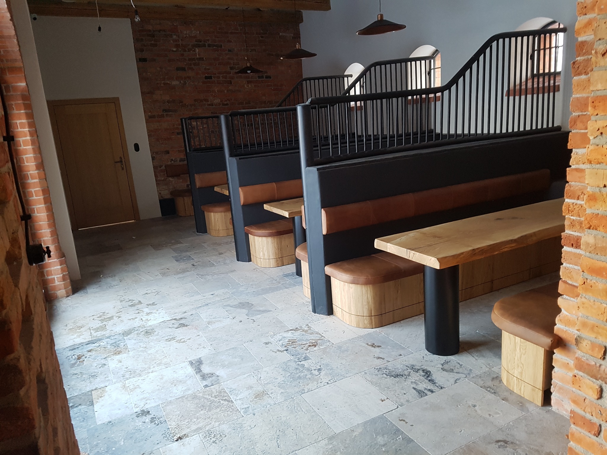 Wykończone wnętrze w Grodźcu z zabudowanymi siedziskami, drewnianymi blatami i ceglanymi ścianami, oświetlone wiszącymi lampami.