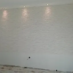 Ściana wykończona dekoracyjną, białą okładziną imitującą kamień, z widocznymi punktowymi źródłami światła w suficie i niedokończonym fragmentem ściany poniżej okładziny.