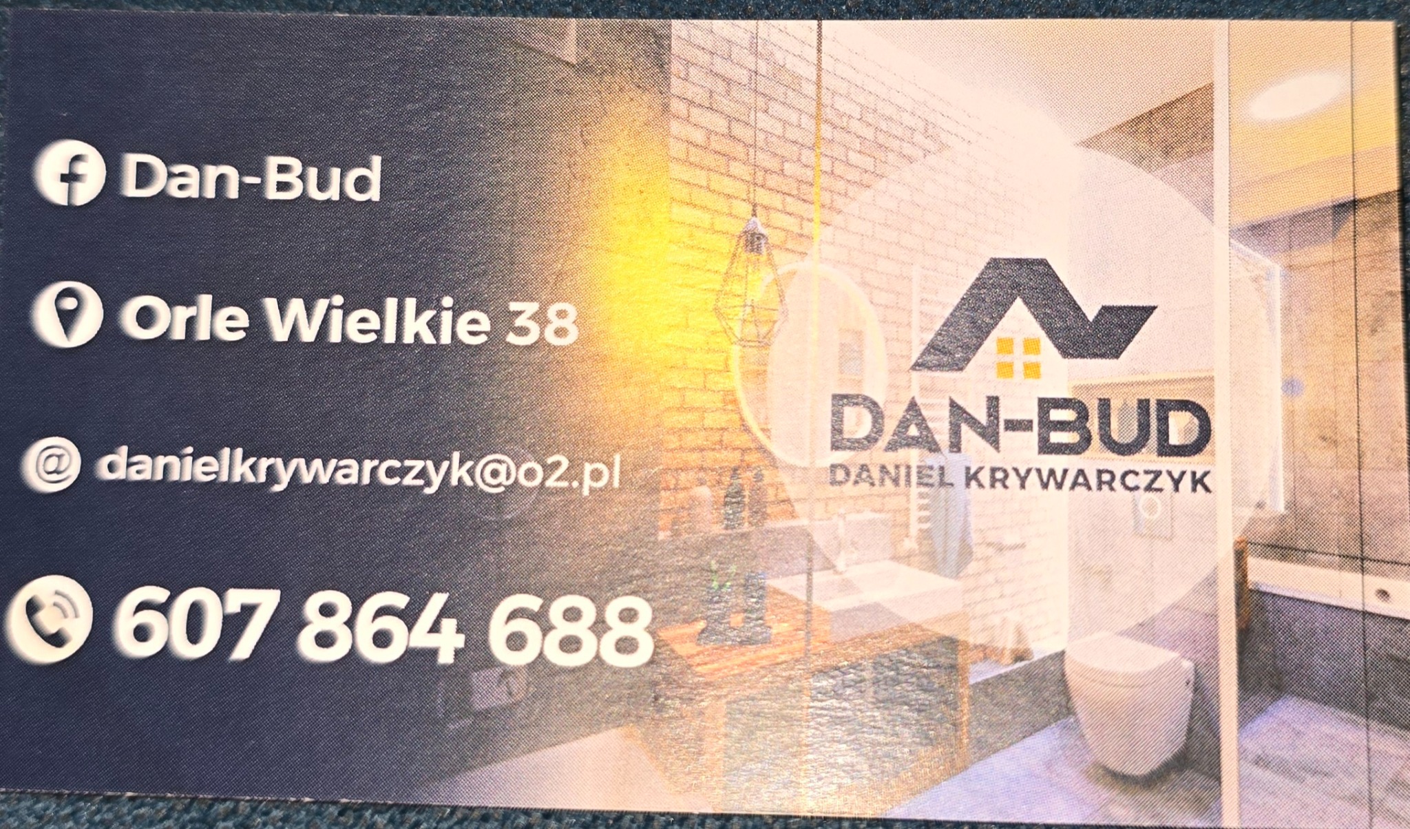 Wizytówka firmy Dan-Bud z adresem, numerem telefonu i adresem email, tło wizytówki przedstawia aranżację wnętrza łazienki z toaletą i kabiną prysznicową.