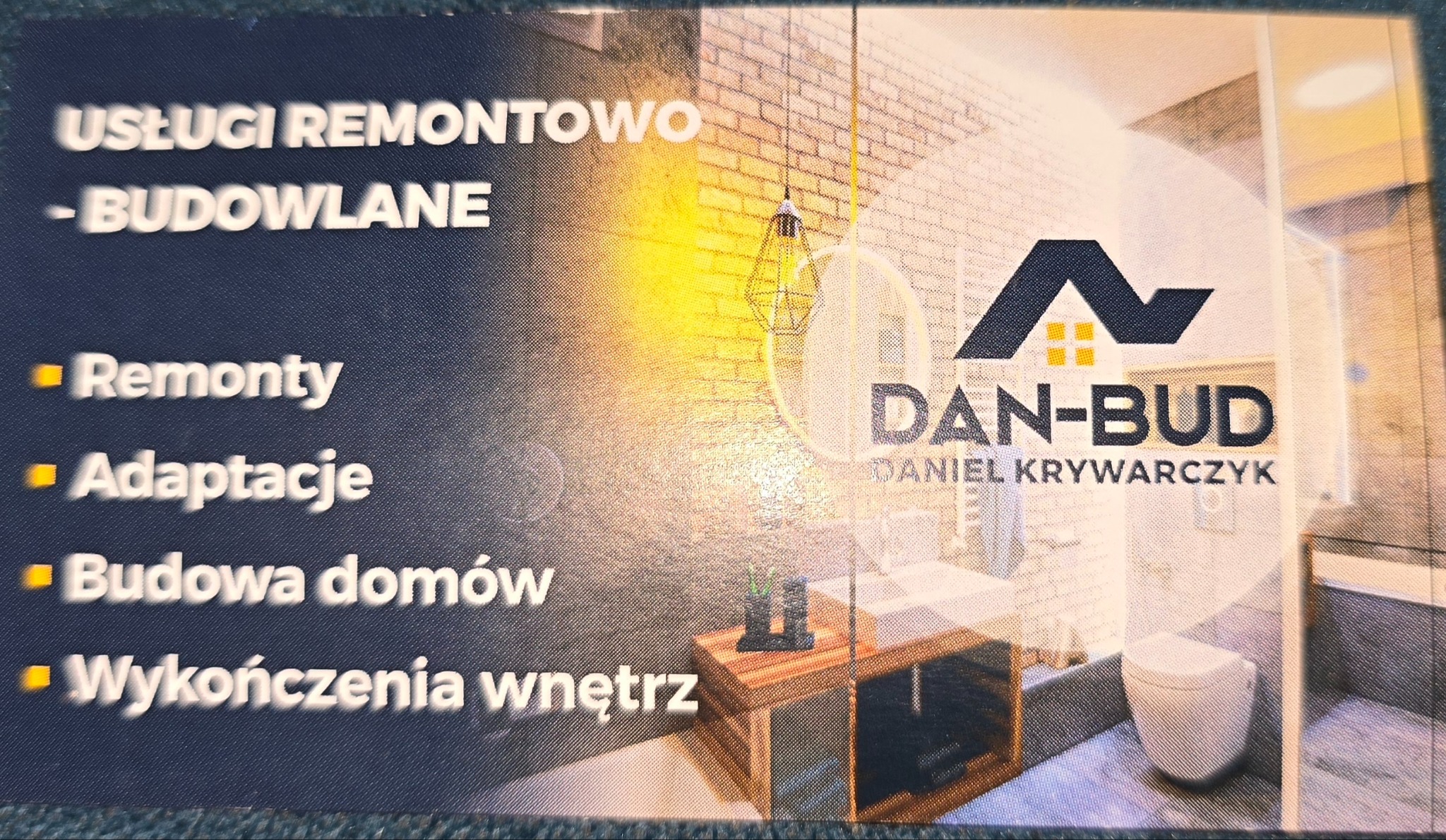 Wizytówka firmy remontowo-budowlanej Dan-Bud Daniela Krywarczyka. Na wizytówce lista usług: remonty, adaptacje, budowa domów, wykończenia wnętrz. W tle wizualizacja łazienki z ceglaną ścianą...
