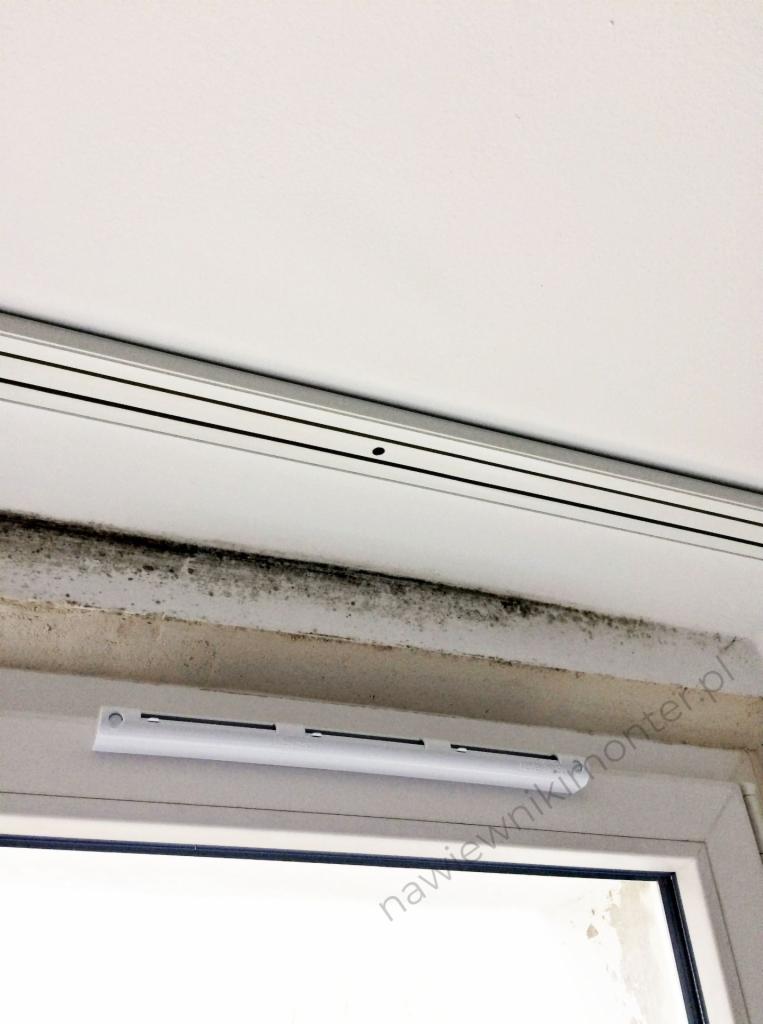 Nawiewnik okienny z widocznym zawilgoceniem i pleśnią na ramie okiennej, białe okno PCV.