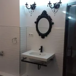 Nowoczesna łazienka z białą armaturą, czarnymi akcentami dekoracyjnymi, wzorzystymi płytkami ściennymi i kabiną prysznicową ze szkła dymionego.