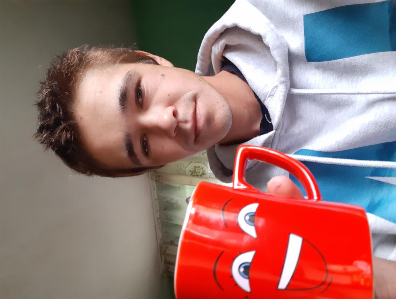 Mężczyzna z czerwoną filiżanką z zabawną buźką, ubrany w bluzę z kapturem, patrzy w obiektyw. Nietypowy kadr i oświetlenie.